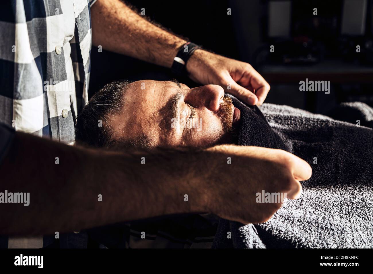 Barbier`s Friseursalon, der das Handtuch dem Kunden ins Gesicht legt. Pre-Shave-Action. Stockfoto